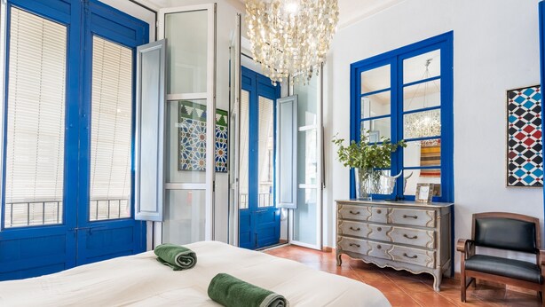 A hotel room with a bed, a dresser, a chair, and a large window with blue shutters. - El Patio Andaluz – House with Pool for Groups (13 Guests) in Vélez-Málaga (Vélez Malaga)