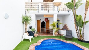 A swimming pool with a white exterior wall, a covered patio area with seating, and potted plants. - El Patio Andaluz – House with Pool for Groups (13 Guests) in Vélez-Málaga (Vélez Malaga)