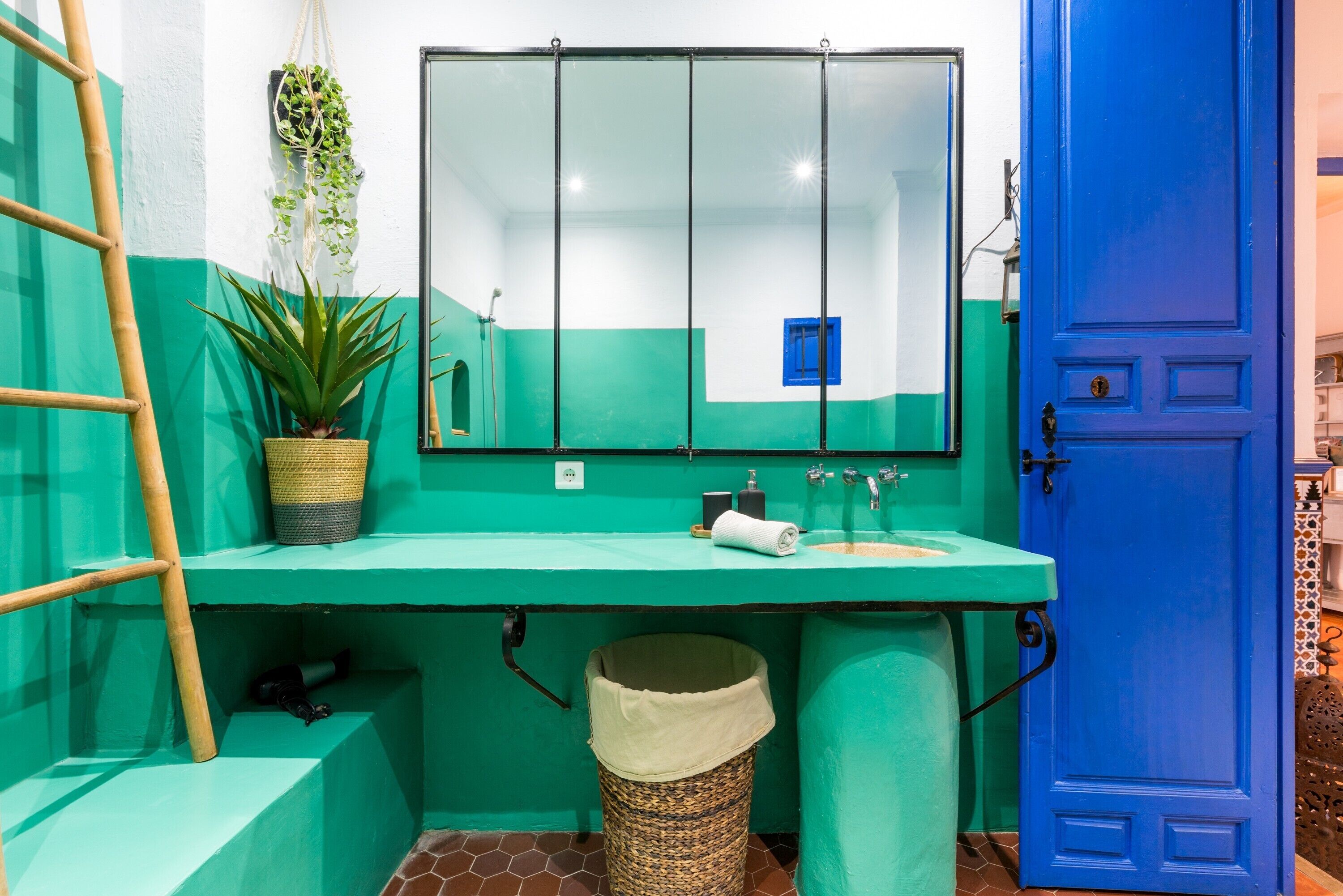 Um banheiro com pia verde, espelho, porta azul e planta em vaso.