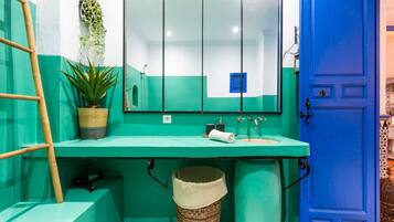 Um banheiro com pia verde, espelho, porta azul e planta em vaso.