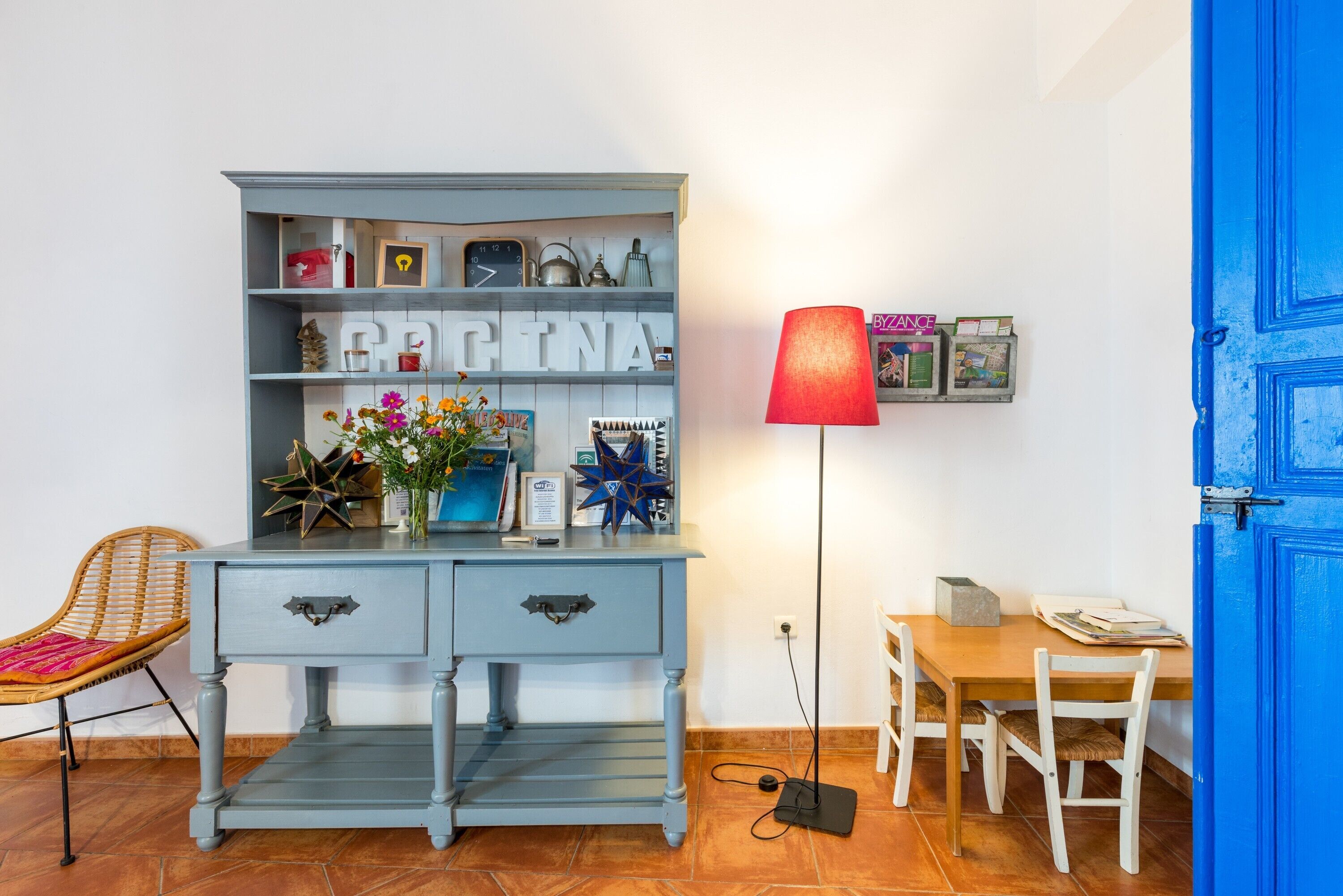 A room with a blue dresser, a red lamp, and a wooden table with chairs.