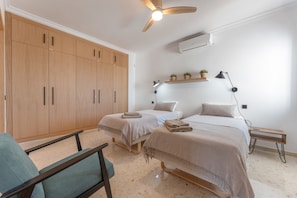 Un dormitorio con dos camas, un ventilador de techo, un armario y una pequeña mesa con lámpara.