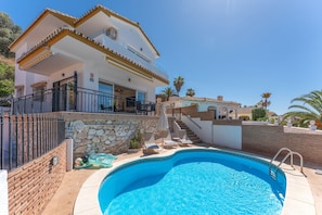 Una casa de dos pisos con piscina, paredes de piedra y un balcón.