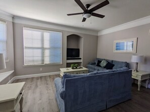 A living room with a blue sofa, a TV, and a ceiling fan.