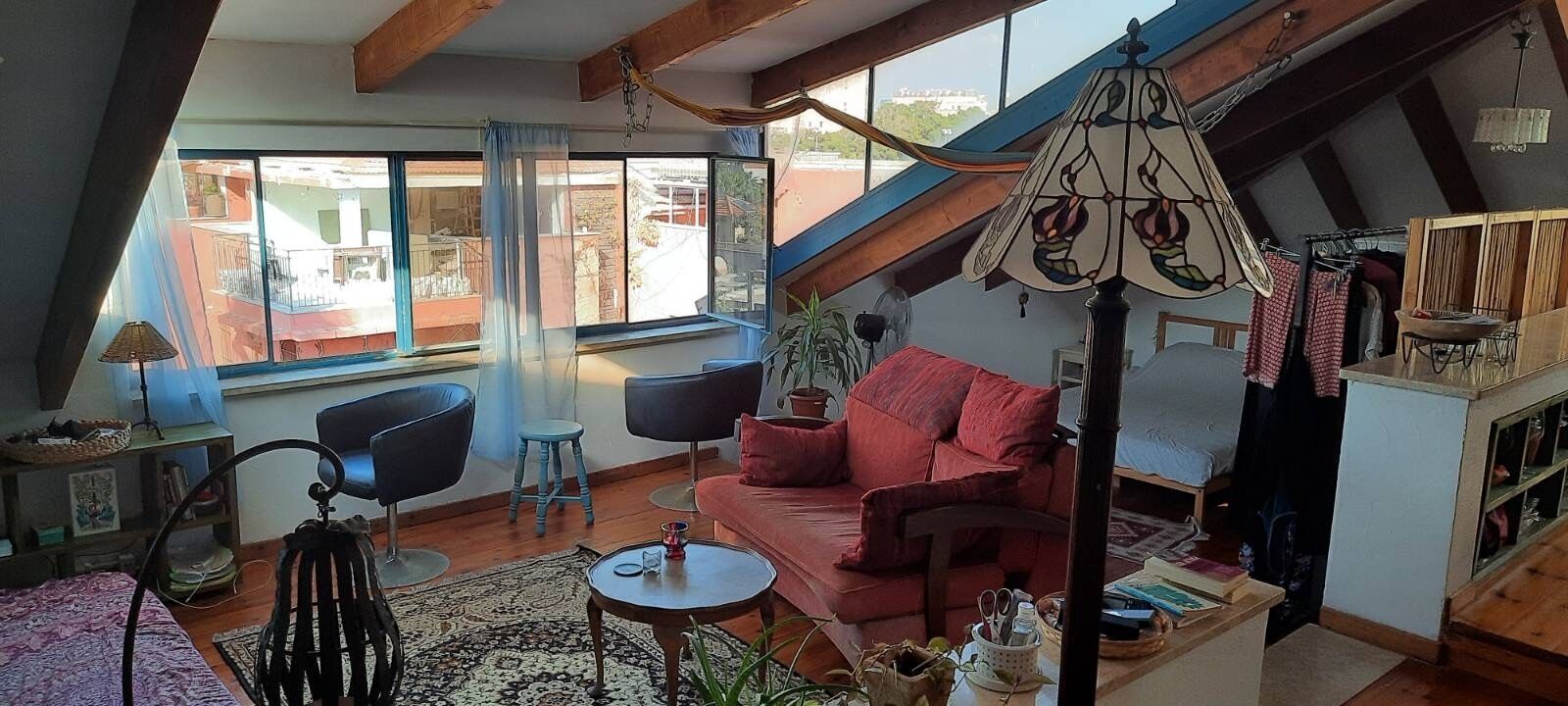 Un salon chaleureux avec un canapé rouge, deux fauteuils noirs, une petite table ronde et une lampe suspendue.