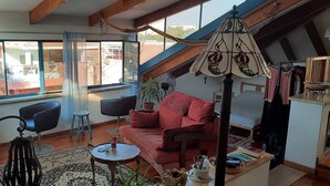 Una sala de estar acogedora con un sofá rojo, dos sillones negros, una mesita redonda y una lámpara colgante.