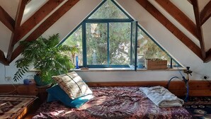 Un dormitorio acogedor en el ático con techo inclinado, un ventanal con vistas a follaje, una cama de madera y un narguilé a la derecha.