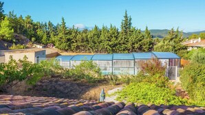 A row of greenhouses with metal frames and blue roofs, surrounded by trees and a hilly landscape. - Sunny Escape to Serenity (Fraissé-Des-Corbieres)