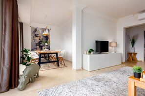 A modern living room with a dining area, a flat-screen TV, white cabinetry, and a large abstract painting.