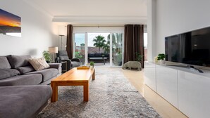 A modern living room with a sofa, coffee table, TV, and a view to the outside. - Apartment 'La Fragata Estepona 3b 2b' with Sea View, Wi-Fi and Air Conditioning (Estepona)