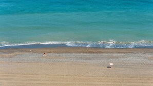 A beach with a pebbly shore, a person sitting, and a beach umbrella. - Apartment 'La Fragata Estepona 3b 2b' with Sea View, Wi-Fi and Air Conditioning (Estepona)