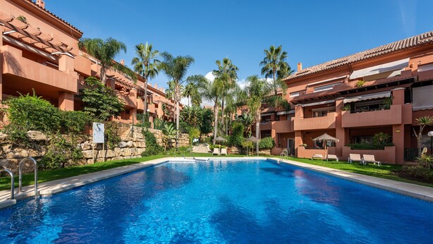 A swimming pool surrounded by multi-story buildings with balconies, palm trees, and a clear blue sky. - Apartment 'La Fragata Estepona 3b 2b' with Sea View, Wi-Fi and Air Conditioning (Estepona)