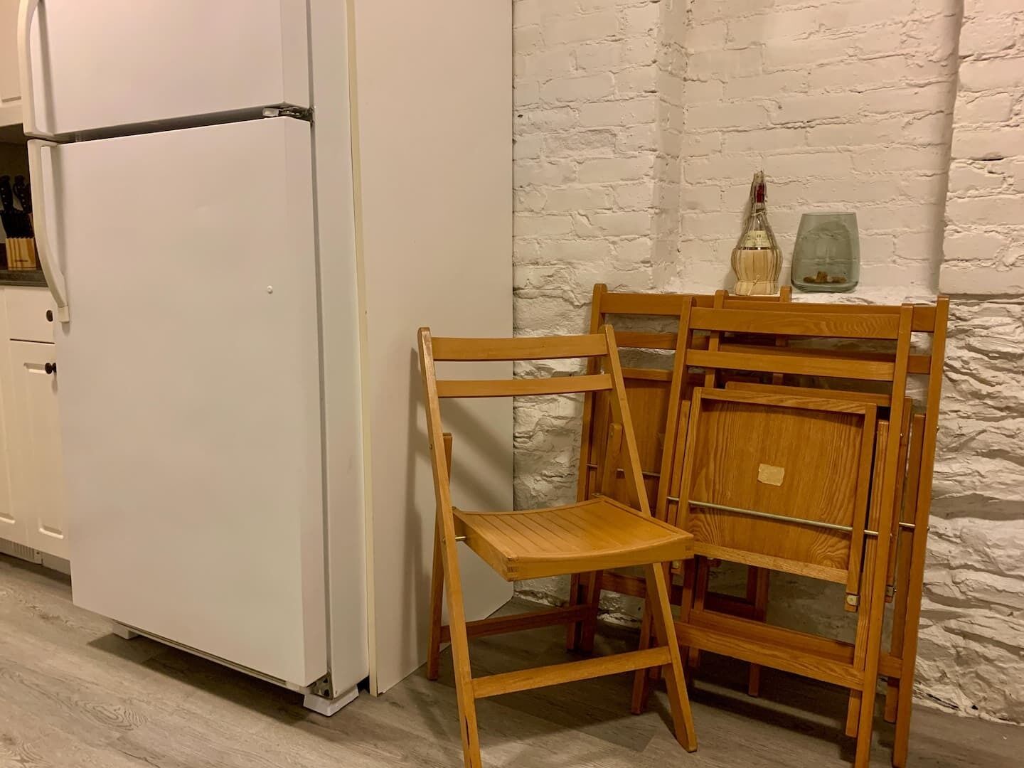 A kitchen with a white refrigerator, wooden chairs, and a white brick wall.