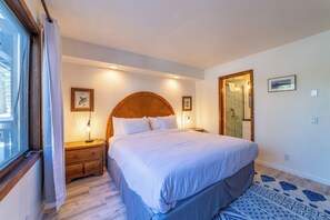 Ein Schlafzimmer mit einem großen Bett, einem Holzkopfteil, Nachttischen mit Lampen und einem Fenster mit Vorhängen.