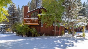 A two-story wooden cabin with a balcony, surrounded by snow-covered trees and a clear sky. - Remodeled Meadowridge Family Retreat! Wifi, Spa (Mammoth Lakes)