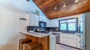 A modern kitchen with white cabinets, a wooden ceiling, and a built-in island with stools. - Remodeled Meadowridge Family Retreat! Wifi, Spa (Mammoth Lakes)