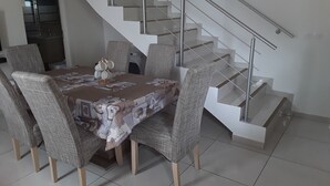 A dining area with a table set for six, surrounded by six chairs. A staircase with a glass railing is visible in the background. - the creolia rue motais in narbonne le tampon  (Le Tampon)