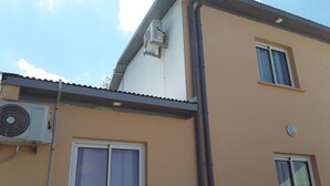 A building with two windows, one with a curtain and another with a screen, and an air conditioning unit mounted on the wall. - the creolia rue motais in narbonne le tampon  (Le Tampon)