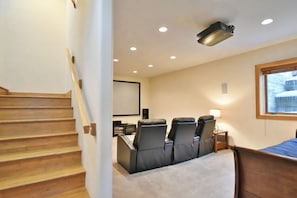 A hotel room with a wooden staircase, a seating area with chairs, a bed, a projector, and a window.