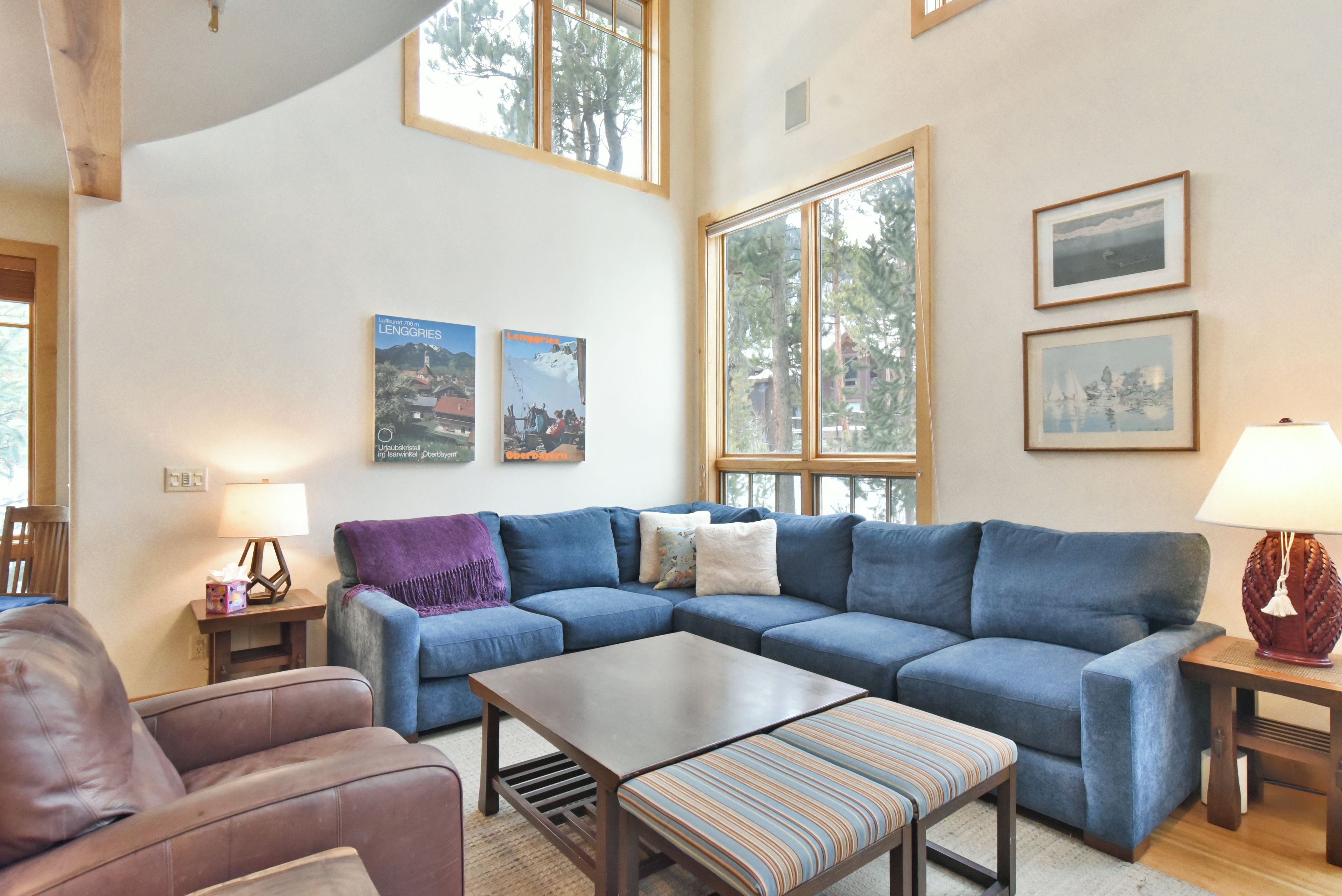 A living room with a blue sofa, a coffee table, and a purple throw blanket. There are two framed pictures on the wall and a lamp on a side table.