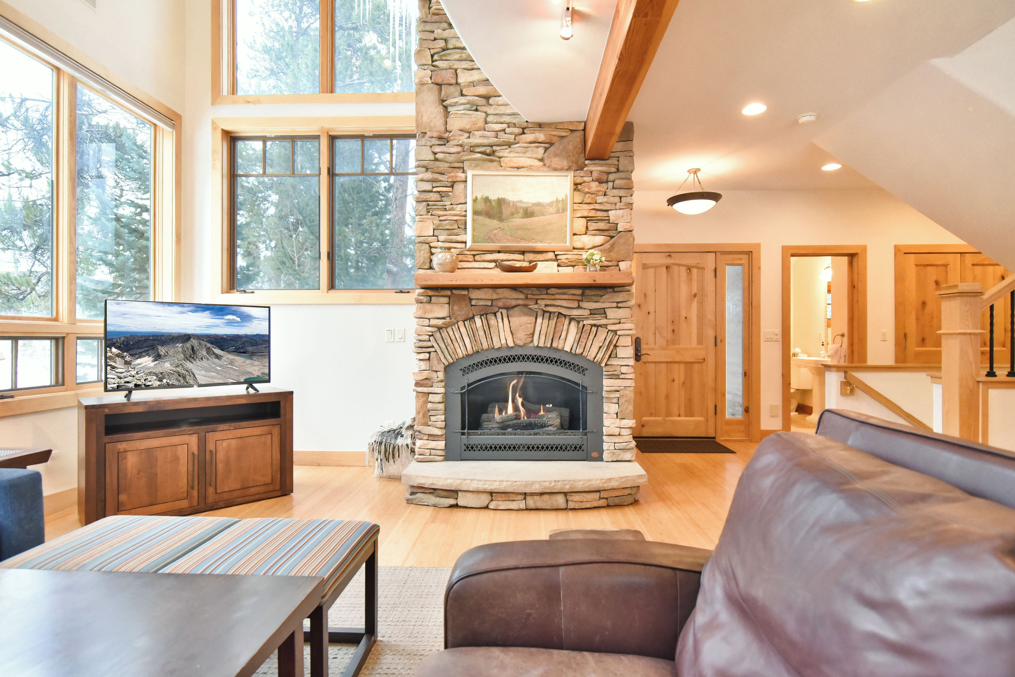 A cozy living room with a stone fireplace, wooden beams, and a television on a wooden cabinet.