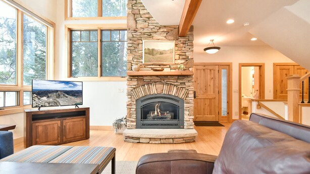 A cozy living room with a stone fireplace, wooden furniture, and large windows offering a view of trees. - Summit Rose Escape • Theater Rm • Gourmet Kitchen (Frisco)
