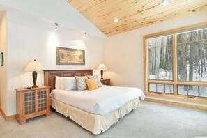 A bedroom with a wooden ceiling, a large window with a view of trees, a bed with white bedding, and two bedside tables with lamps. - Summit Rose Escape • Theater Rm • Gourmet Kitchen (Frisco)