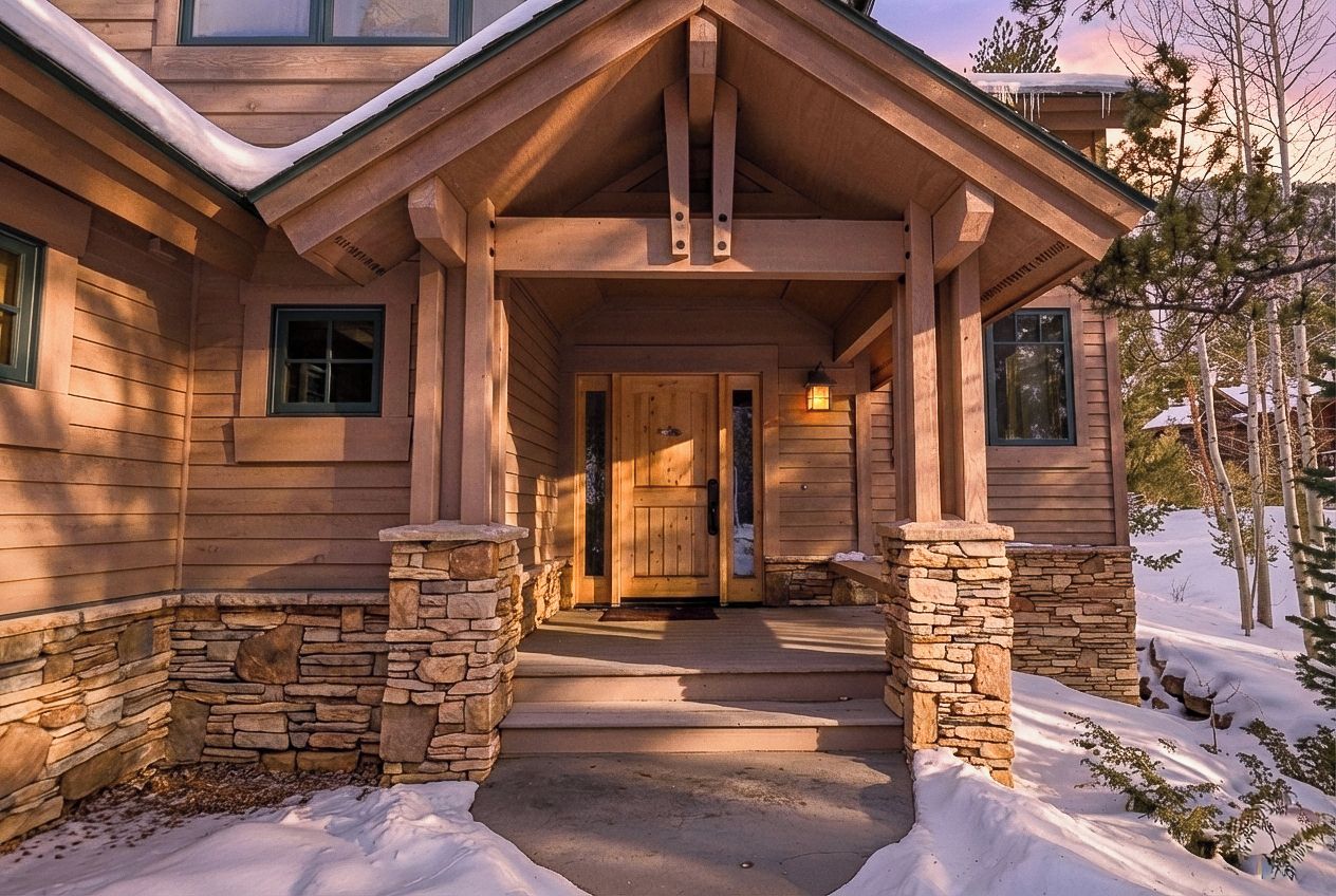 Una casa de madera con cimientos de piedra, un porche y una puerta.