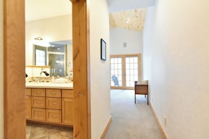 A hallway leading to a bathroom with a large mirror, wooden cabinets, and a shower area.