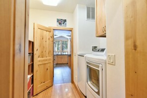Un pasillo estrecho con puertas de madera, una lavadora y un ventanal que da a un balcón.