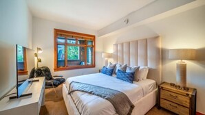 A bedroom with a large bed, bedside tables, a desk, and a window with a view of greenery. - Capitol Peak Lodge 3306 (Snowmass)
