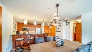 A modern kitchen with wooden cabinets, a stainless steel refrigerator, and a bar area with stools. - Capitol Peak Lodge 3306 (Snowmass)