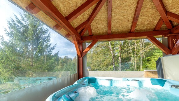 Een hottub onder een houten constructie met uitzicht op bomen.