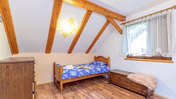 A bedroom with a wooden ceiling, a bed with a floral bedspread, a wooden dresser, and a window with sheer curtains.