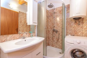 A bathroom with a sink, shower, and washing machine.