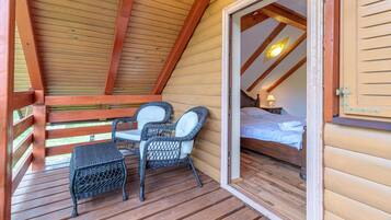A wooden cabin with a balcony, wicker chairs, a bed, and a nightstand.