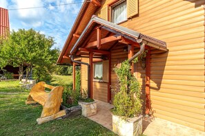 A wooden log cabin with a porch, a stone bench, and a small garden.