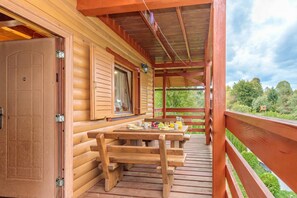 A wooden deck with a table set for breakfast, a door, and a window with shutters.
