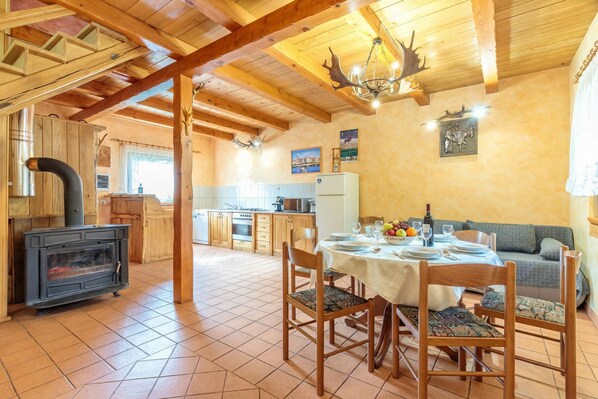 Un interior rústico con una mesa de comedor para cuatro personas, vigas de madera en el techo, una zona de cocina y una chimenea.