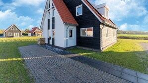 Ett modernt hus med ett brant tak, en stor veranda och en välskött gräsmatta.