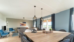 Ett modernt vardagsrum med ett stort matbord i trä, grå stoppade stolar, en soffa och en tv.