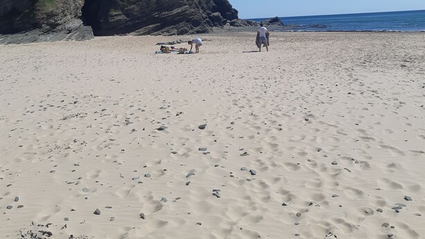 Ein sandiger Strand mit steinigen Klippen und blauem Himmel.