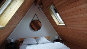 Ein dreieckiger Raum mit Holzwänden, einem Bett mit weißer Bettwäsche, zwei Nachttischen mit Lampen und einem Oberlicht.