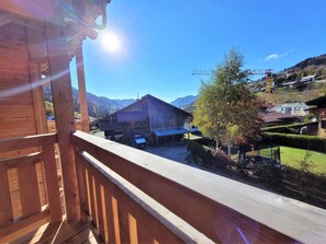Un balcón de madera con vistas a una zona rural, con una montaña al fondo, un granero y cielo despejado.