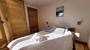 A neatly made bed with a folded towel, a wooden door, and a framed picture on the wall. - Bright 5-room apartment, comfort for 8 people, garage included (Les Gets)