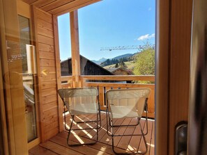 A wooden balcony with two metal chairs, a wooden door, and a view of a mountain landscape with a bridge. - Bright 5-room apartment, comfort for 8 people, garage included (Les Gets)