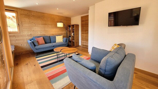 A modern living room with a blue sofa, a smaller sofa, a coffee table, and a bookshelf. - Bright 5-room apartment, comfort for 8 people, garage included (Les Gets)