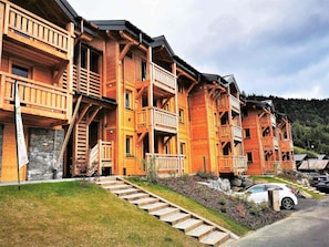 Une rangée de chalets en bois dotés de balcons, reposant sur des fondations en pierre, avec une voiture garée devant.