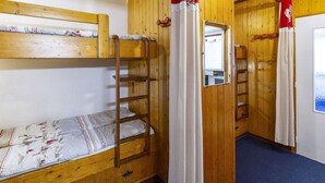 Quarto com beliches, paredes de madeira, escada e cortinas.