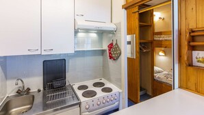 Uma cozinha compacta com armários brancos, fogão, pia e despensa de madeira.